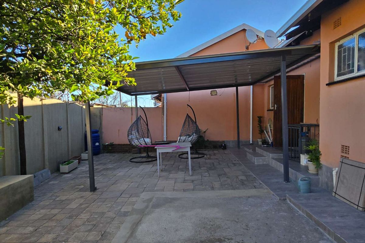 A rear exterior view of the townhouse featuring a paved patio area covered by a metal roof structure and enclosed by boundary walls.