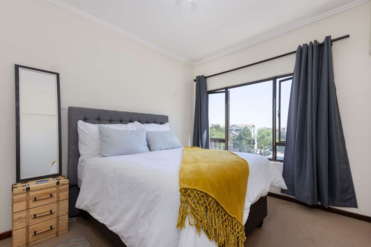 A well-lit bedroom featuring carpeted flooring, a large window with curtain fixtures, and neutral wall finishes.