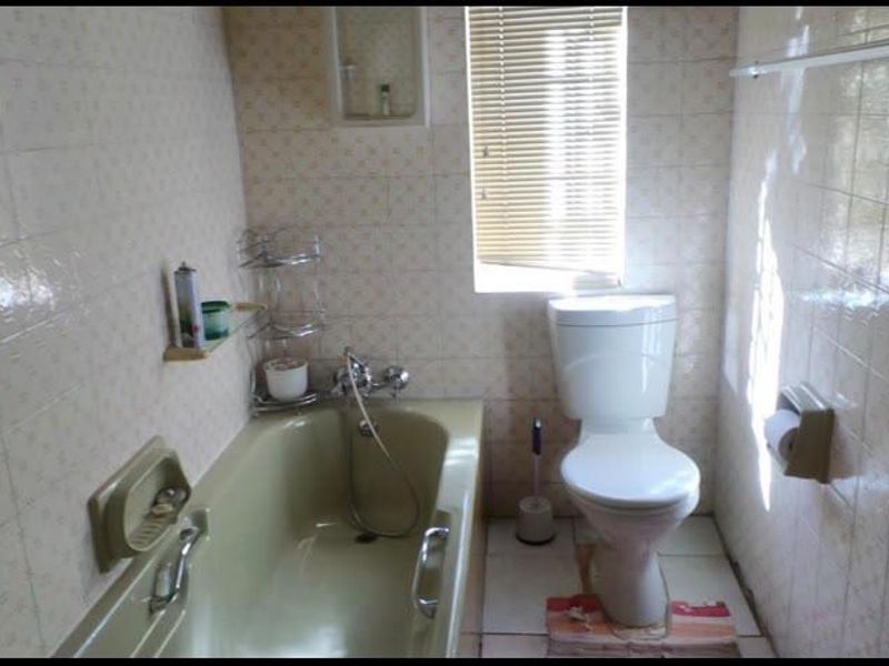 A compact bathroom featuring dated wall tiles, a bathtub with integrated shower mixer, and a standard toilet.