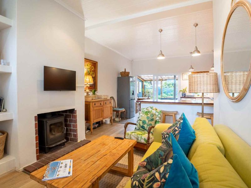Open-plan living area featuring a wood-burning stove with brick surround, built-in shelving, and a kitchen island, flowing towards a rear patio.
