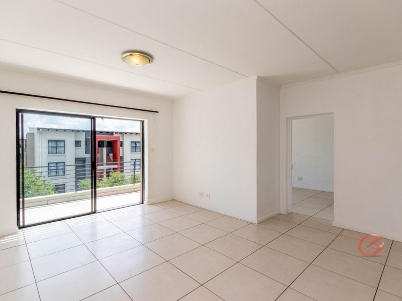 Bright and spacious open-plan living area featuring neutral ceramic floor tiles and a large sliding glass door leading to a private balcony.