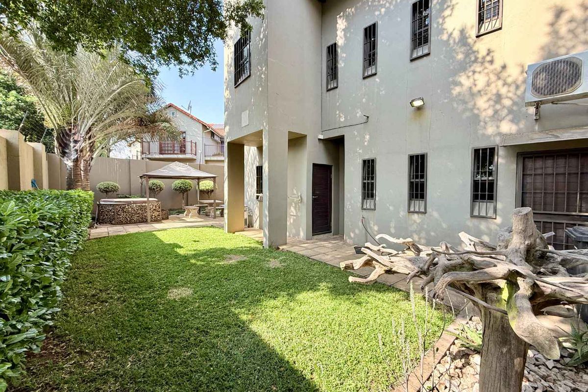 A private rear garden featuring a paved patio area, well-maintained lawn, and secure boundary walls, providing a functional outdoor space for the townhouse.