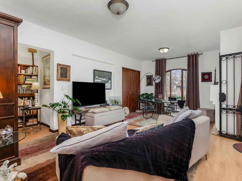 A comfortable living room featuring laminate flooring, built-in shelving, and an arched window with access to a secure wrought iron entrance door.