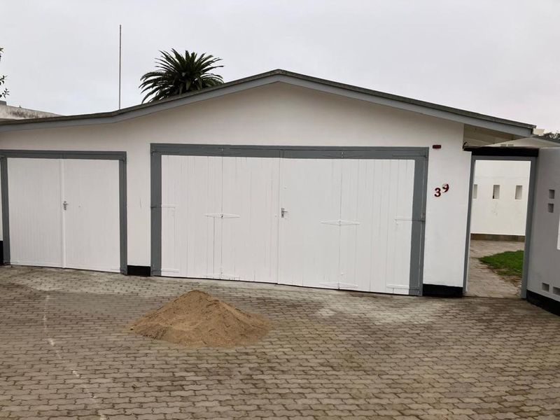 Exterior view of a double and single garage with white doors and grey trim, featuring a paved driveway and side pedestrian access.