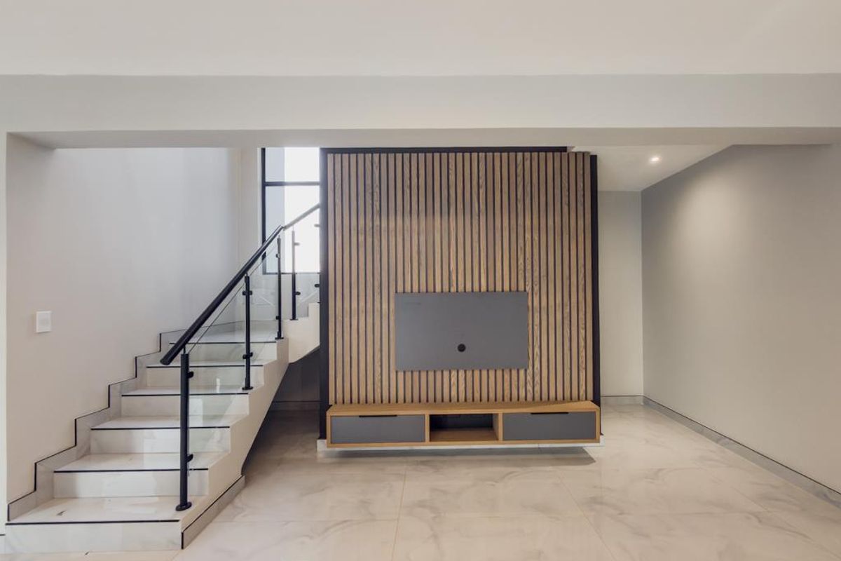 Modern living area featuring a striking timber slat feature wall, built-in media console, and a sleek staircase with glass balustrades and marble-look tiled flooring.