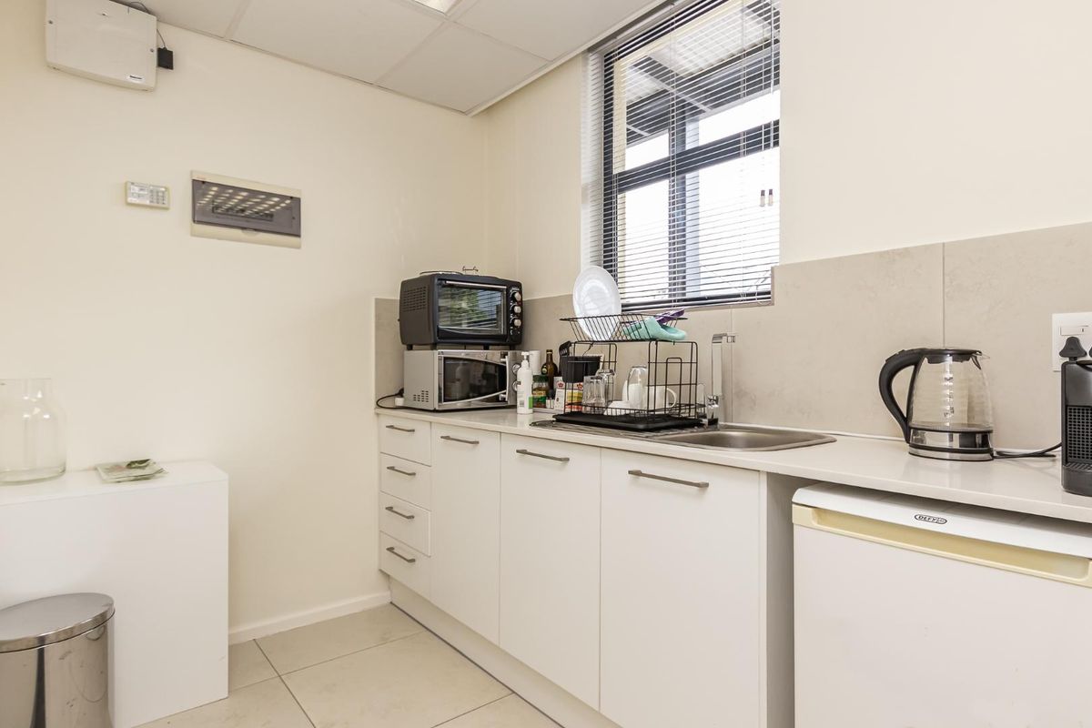 A compact kitchenette featuring white cabinetry, a stainless steel sink, tiled splashback, and a drop ceiling with integrated lighting.