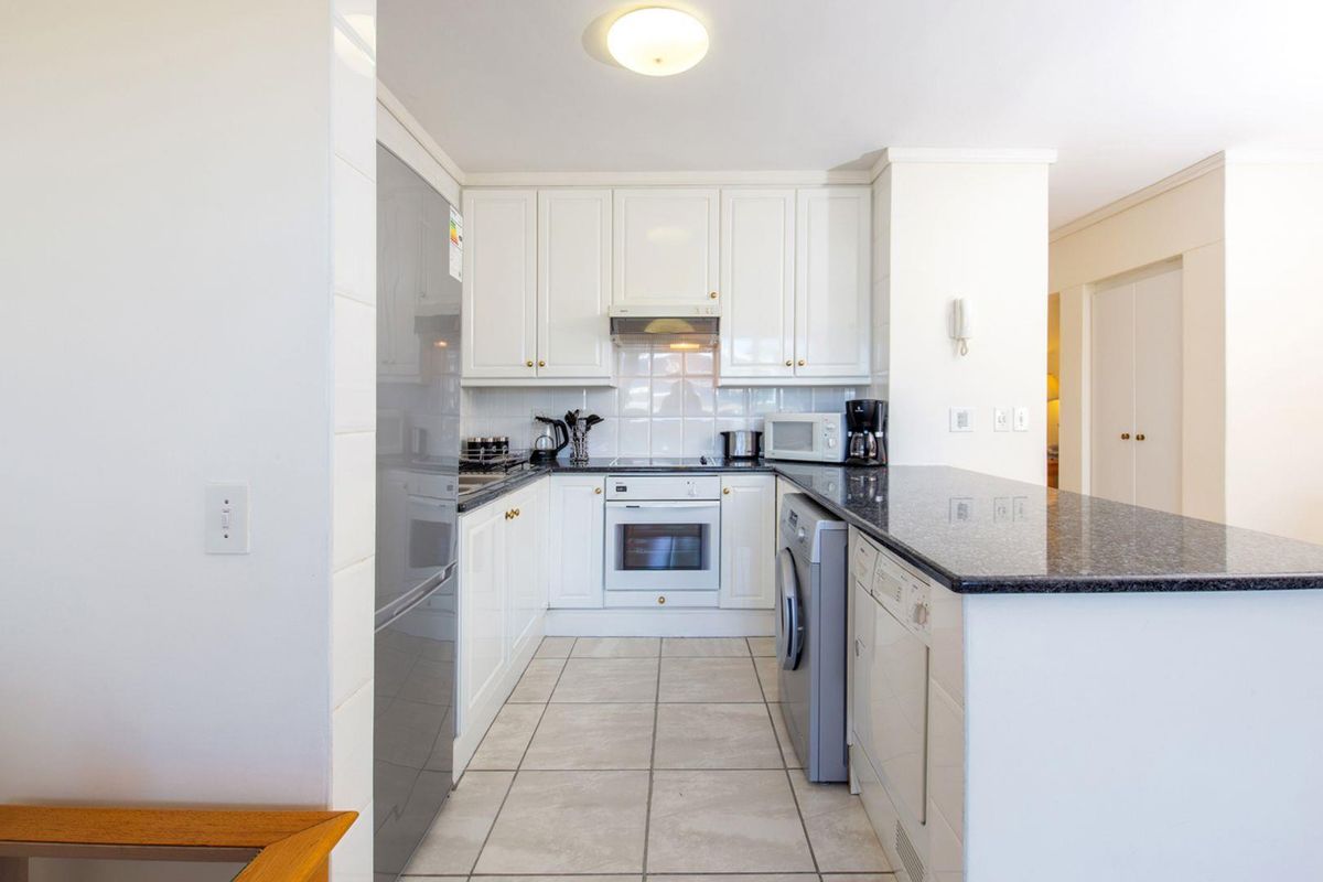 A functional kitchen featuring white cabinetry, granite countertops, built-in oven, electric cooktop, and a breakfast bar, with tiled flooring throughout.