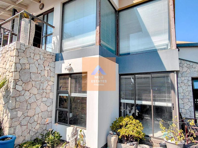Rear exterior view of the property featuring stone cladding, large aluminium-framed windows, and an upper-level balcony.