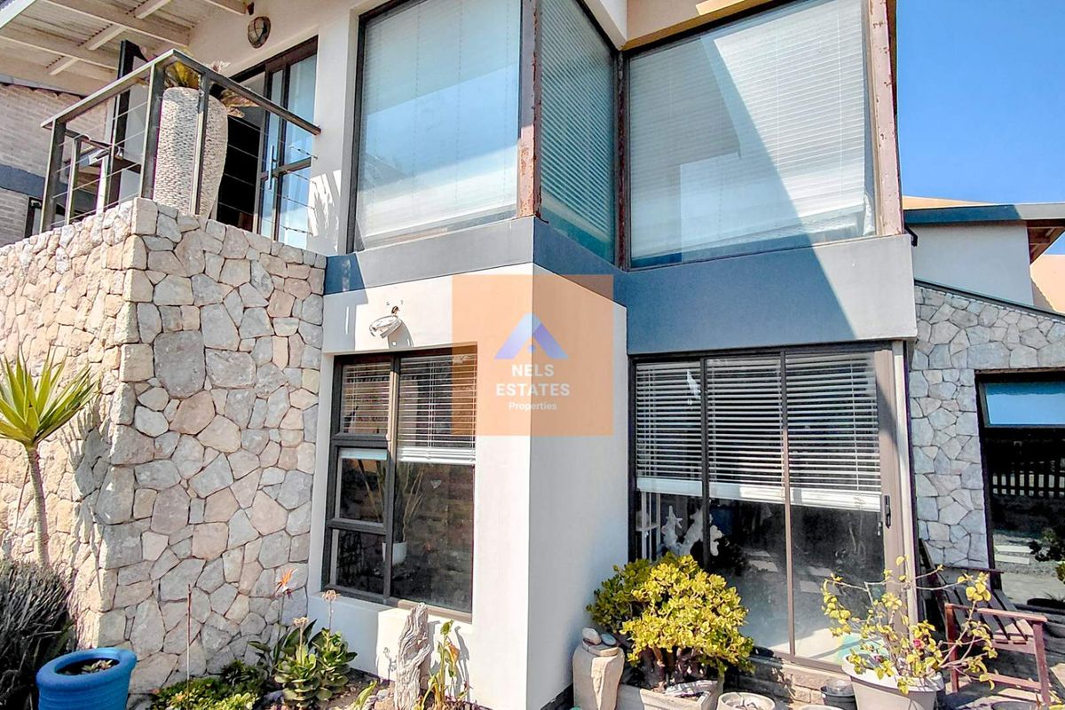 Rear exterior view of the property featuring stone cladding, large aluminium-framed windows, and an upper-level balcony.