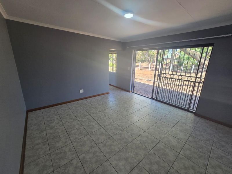 An empty living room featuring grey walls, tiled flooring, and a sliding glass door with an integrated security gate leading to the exterior.