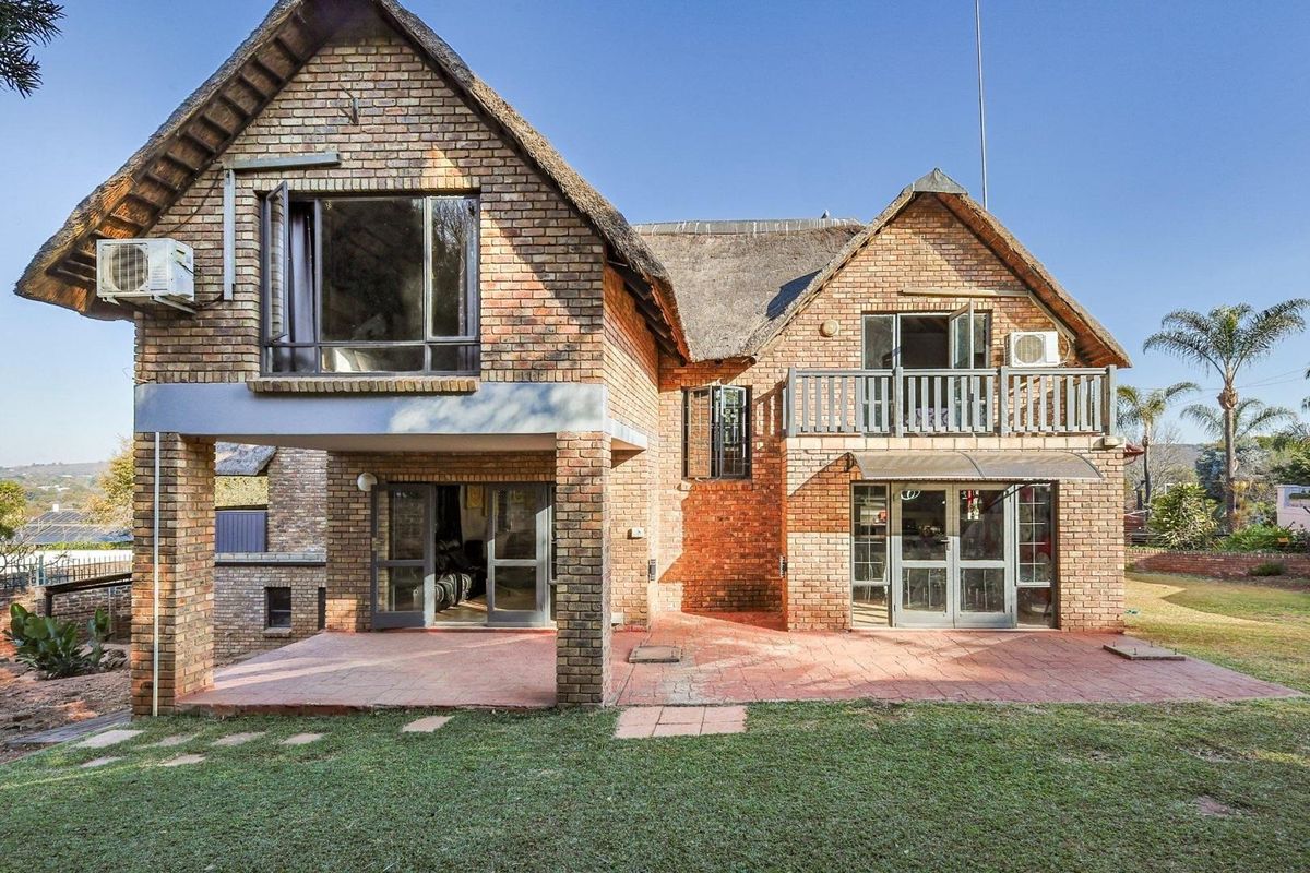 Rear view of a double-story face brick house featuring a thatched roof, covered patio, balcony, and a spacious garden area.