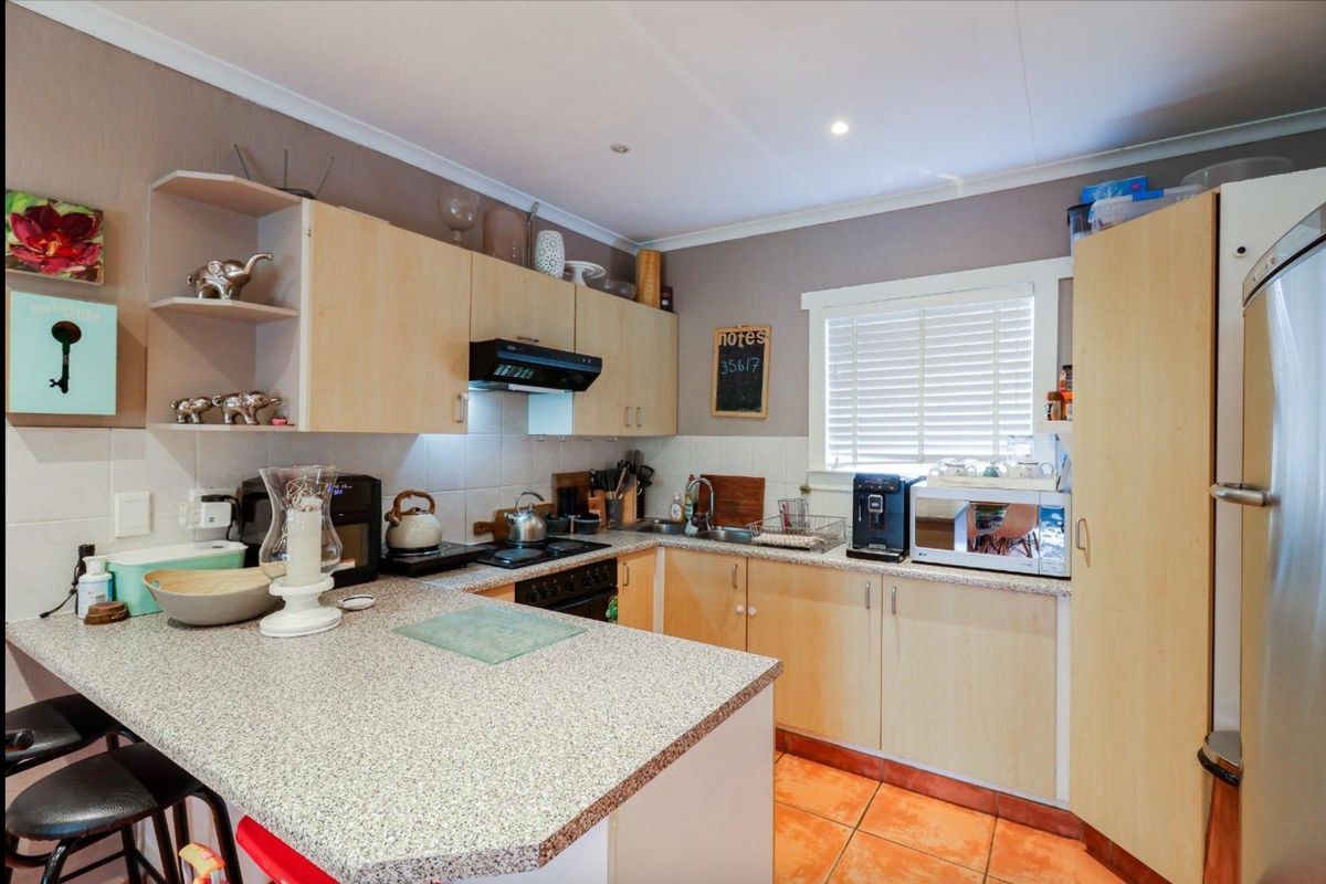 A functional kitchen featuring light wood cabinetry, granite-look countertops, a built-in hob with extractor fan, and tiled flooring.