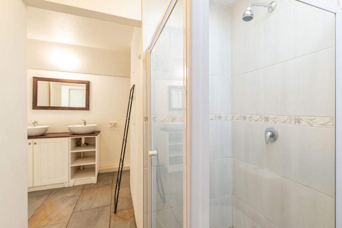 A bright bathroom featuring a double vanity with vessel sinks, tiled flooring, and a separate shower enclosure with wall tiling.