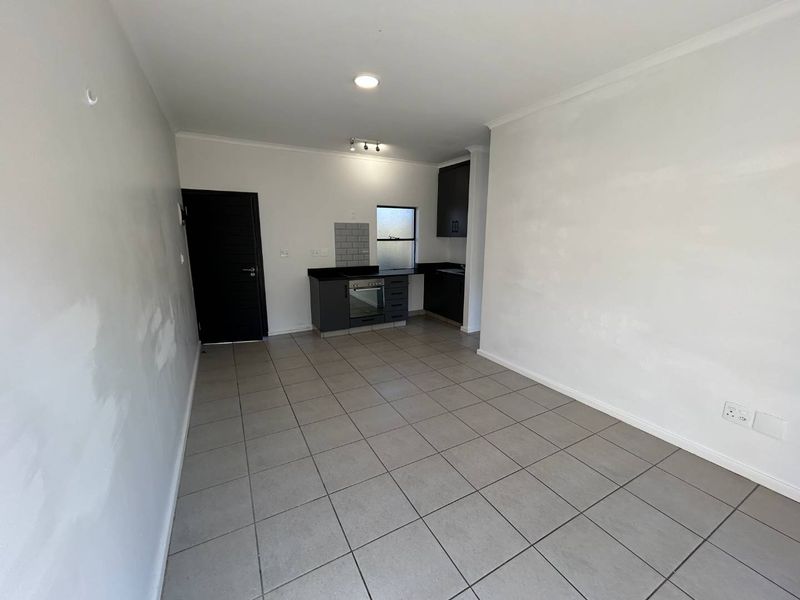 Open plan kitchen and living area featuring tiled flooring, dark cabinetry with granite countertops, and built-in oven, presenting a clean, blank canvas for customization.