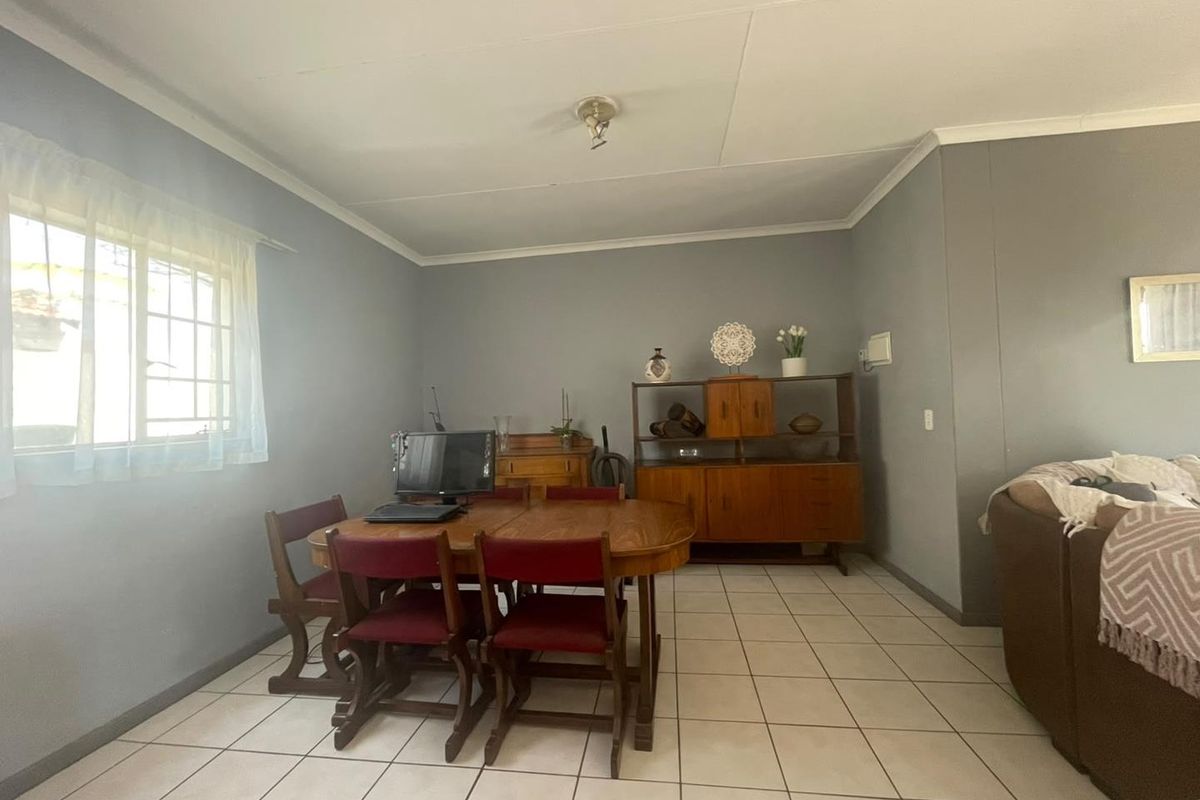 A functional living area featuring neutral grey walls, tiled flooring, and a window fitted with security bars.
