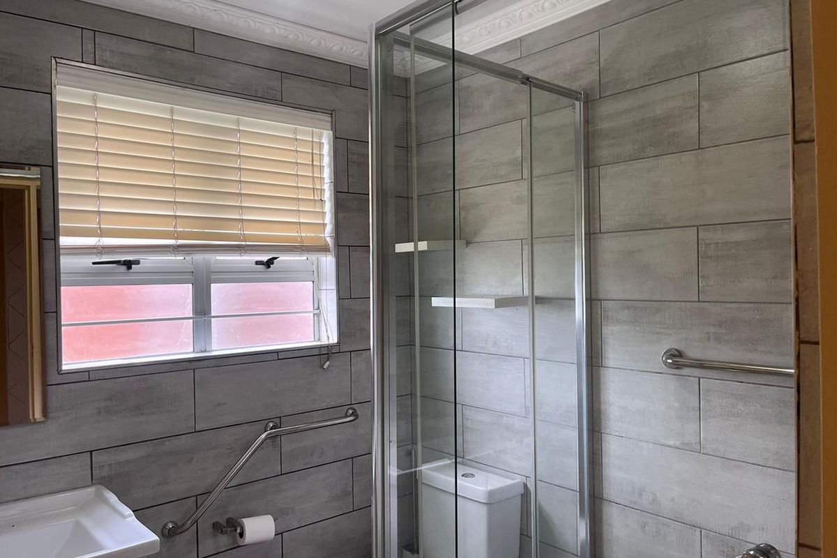 A modern bathroom featuring grey ceramic wall tiles, a glass shower enclosure, and installed safety grab rails for accessibility.