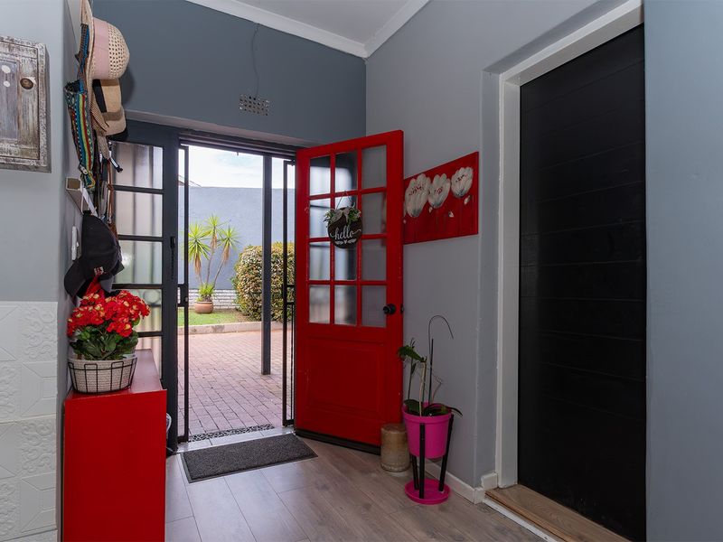 Welcoming entrance hall featuring laminate flooring and a vibrant red glass-panelled door leading to the outdoor patio area.