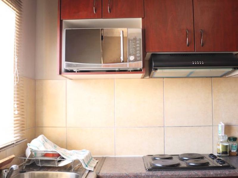 A functional kitchen featuring dark wood cabinetry, laminate countertops, a built-in oven with electric hob, extractor fan, and a double bowl stainless steel sink.