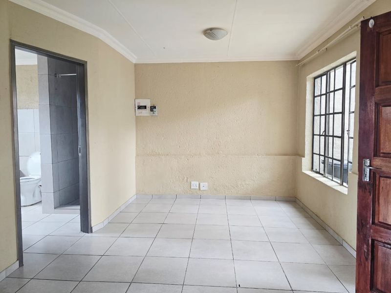An empty living area featuring tiled flooring, burglar bars on the window, and direct access to an adjacent bathroom.