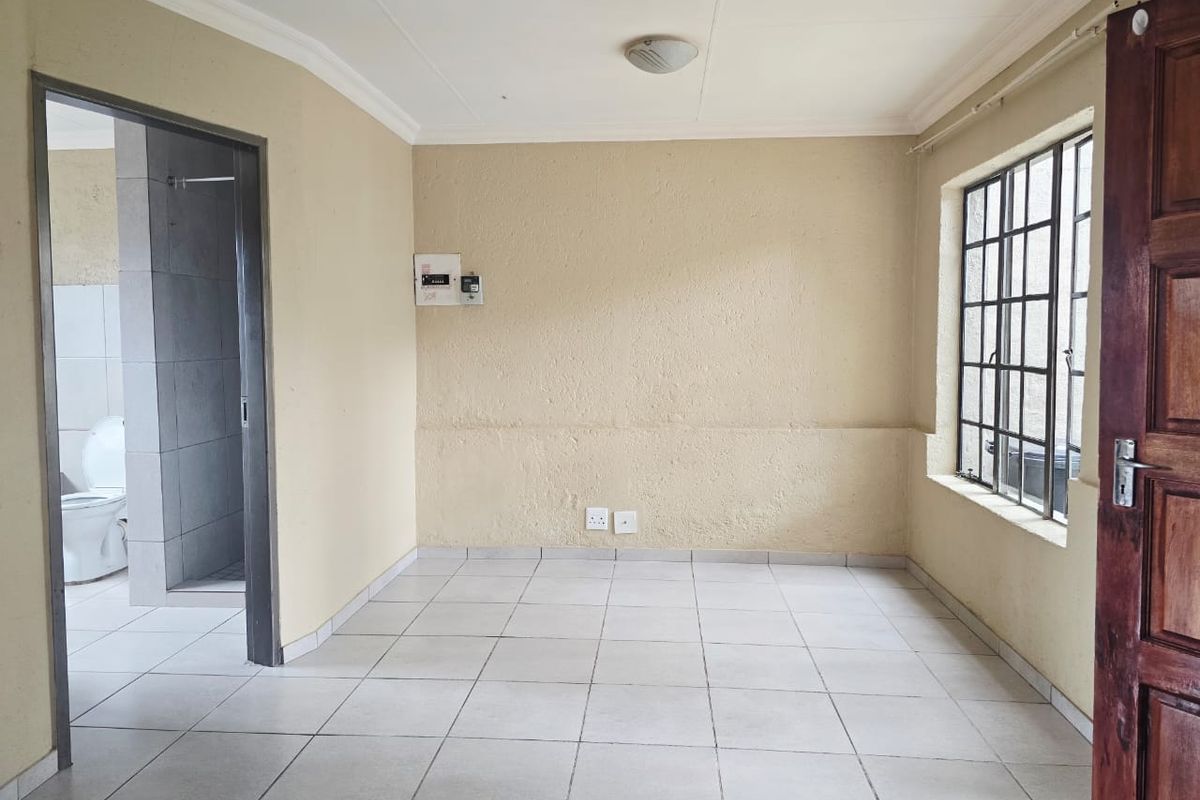 An empty living area featuring tiled flooring, burglar bars on the window, and direct access to an adjacent bathroom.