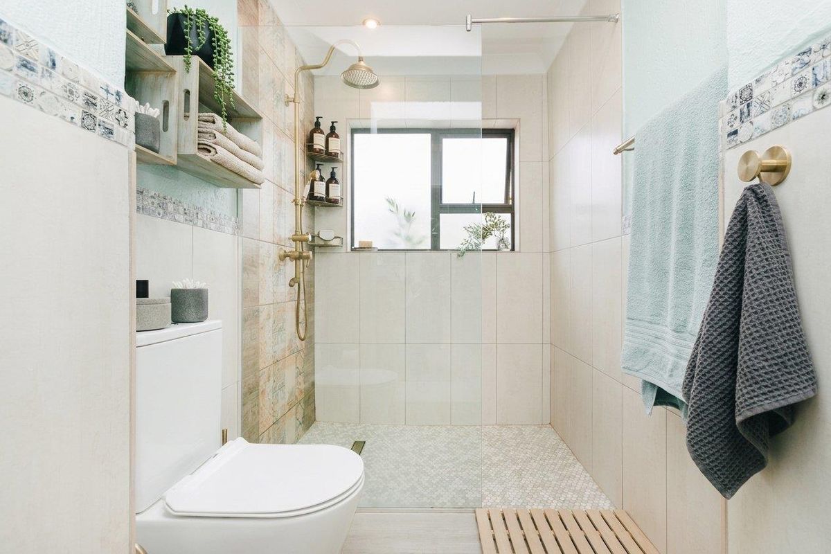 Modern bathroom featuring a walk-in shower with brass fixtures, mosaic floor tiling, wall-mounted toilet, and neutral wall tiles.