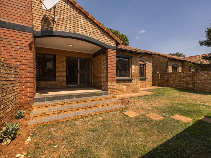 Rear view of a face brick townhouse featuring a covered patio with tiled steps, a small private garden, and secure sliding door access.