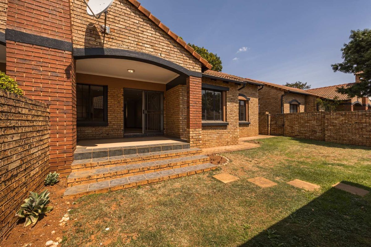 Rear view of a face brick townhouse featuring a covered patio with tiled steps, a small private garden, and secure sliding door access.