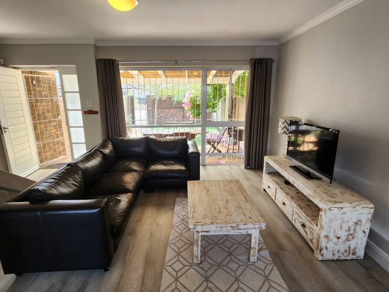 A bright living room featuring laminate flooring, a staircase, and a large sliding glass door providing direct access to the outdoor patio area.