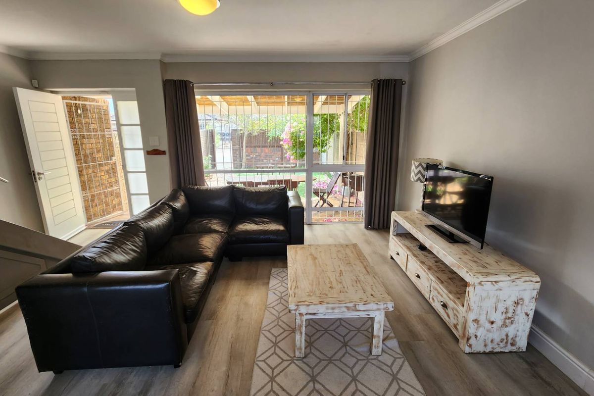 A bright living room featuring laminate flooring, a staircase, and a large sliding glass door providing direct access to the outdoor patio area.