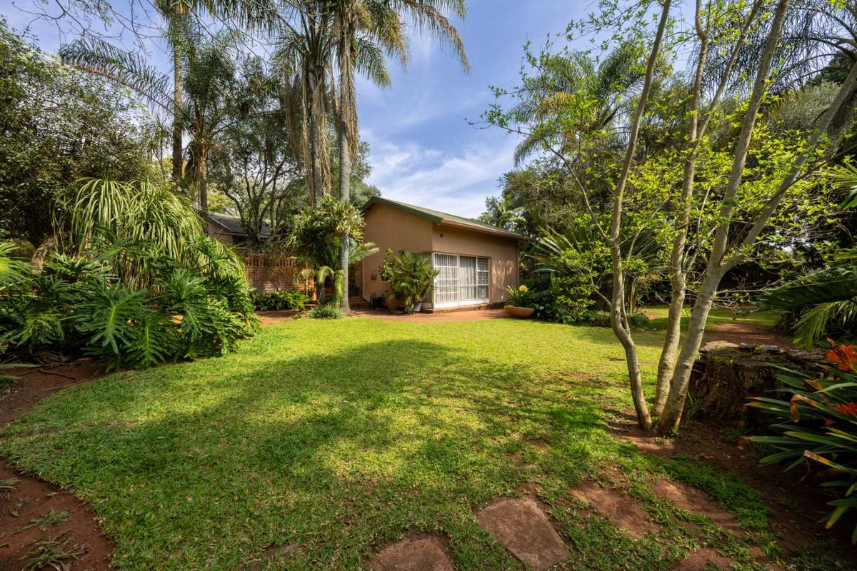 A view of the rear exterior of the house, featuring a well-maintained lawn, mature trees, and a sliding glass door entrance.