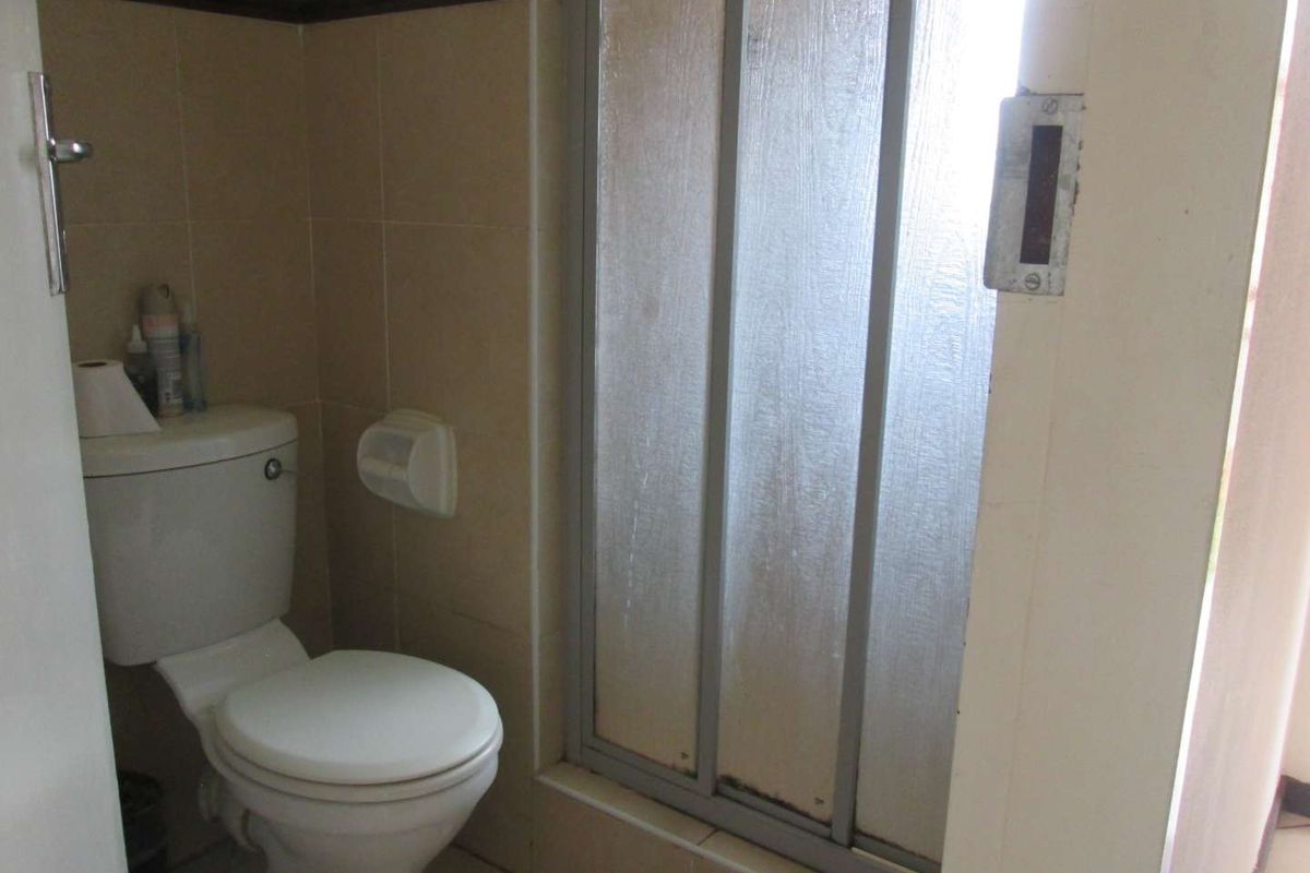 A compact bathroom featuring a standard toilet and a shower enclosure with a sliding door, finished with neutral wall tiling.