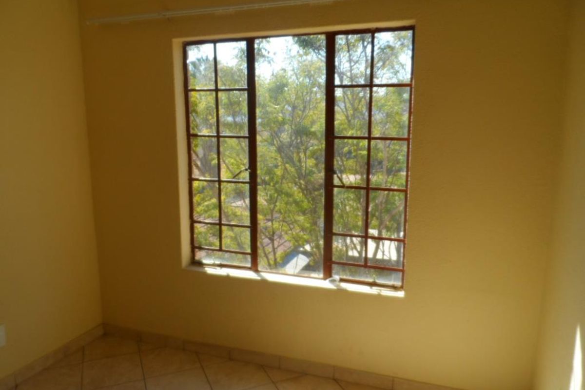 A vacant bedroom featuring tiled flooring and a large window with metal frames, offering a view of the surrounding trees.
