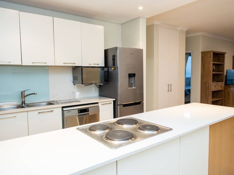 Modern kitchen featuring white cabinetry, stone countertops, a central island with an electric cooktop, and integrated appliances.