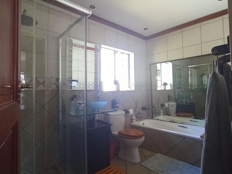 A functional bathroom featuring a glass shower enclosure, a bathtub, a vessel sink vanity, and tiled finishes throughout.