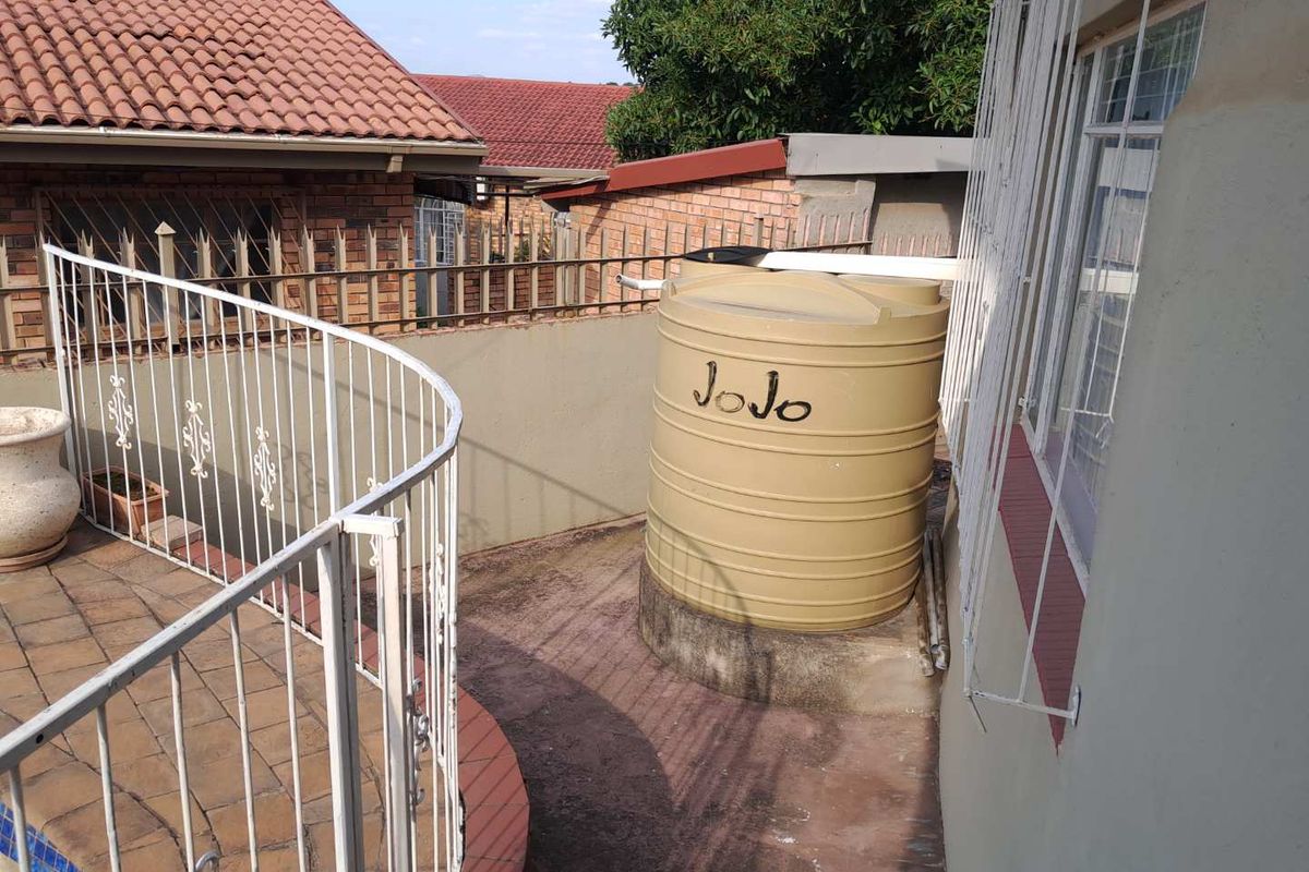 Rear exterior area featuring a water storage tank, paved patio space, and security fencing.
