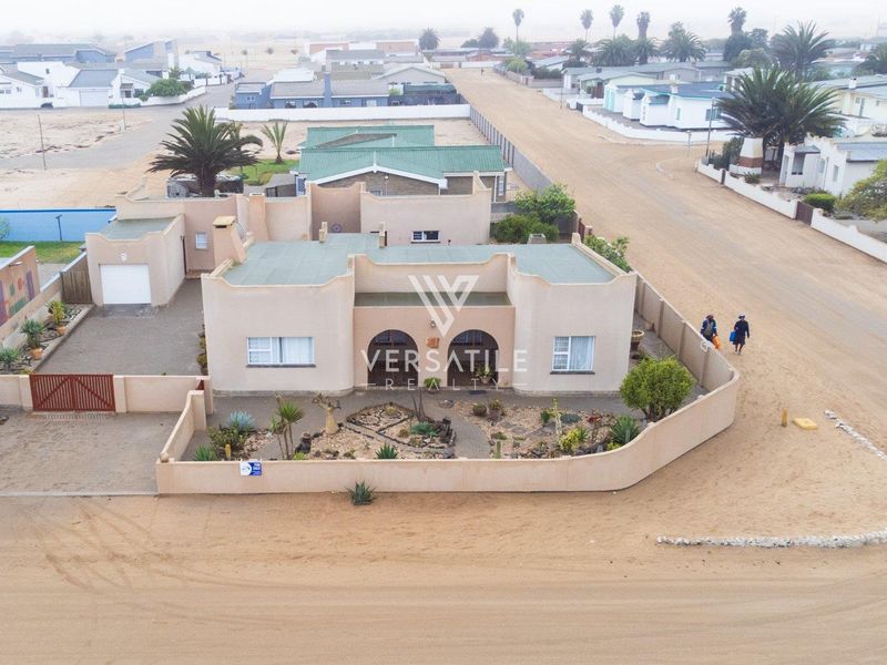 Aerial view of a residential property featuring a walled garden, driveway, and garage in a coastal neighborhood setting.