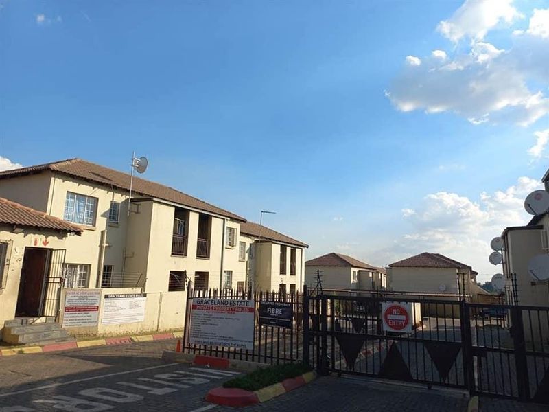 Front entrance view of a townhouse complex featuring security gates, paved driveway access, and multi-unit residential buildings.