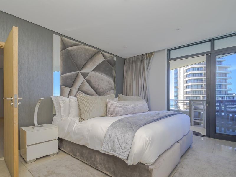 Modern bedroom featuring a textured feature wall, recessed lighting, and large sliding glass doors leading to a private balcony with city views.