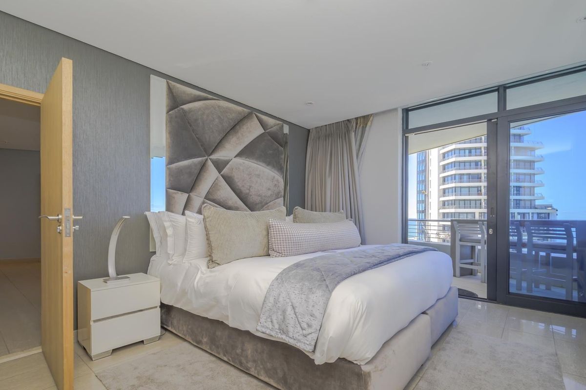 Modern bedroom featuring a textured feature wall, recessed lighting, and large sliding glass doors leading to a private balcony with city views.