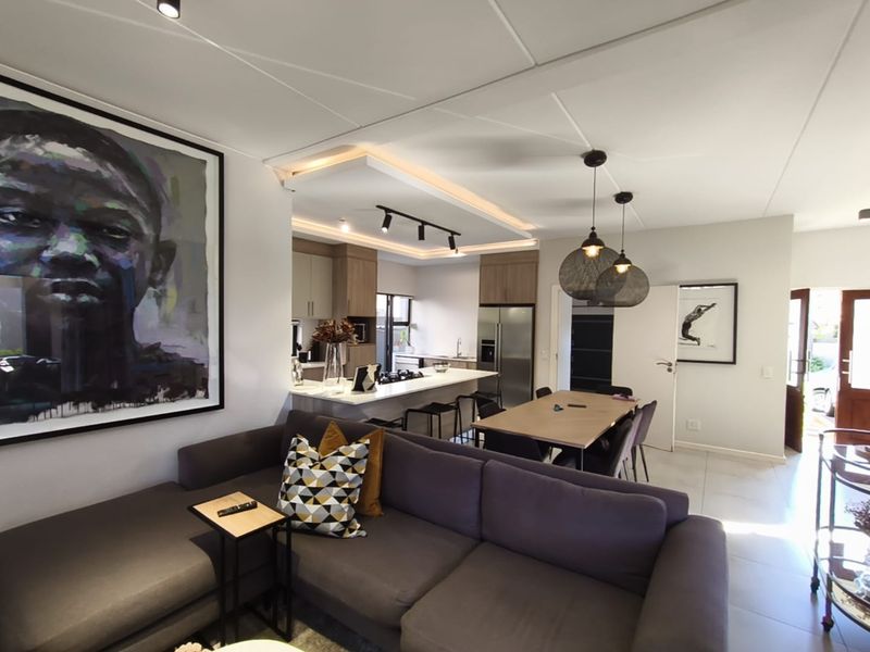 Modern open-plan living and dining area featuring a sleek kitchen with a central island, contemporary lighting, and neutral tiled flooring throughout.