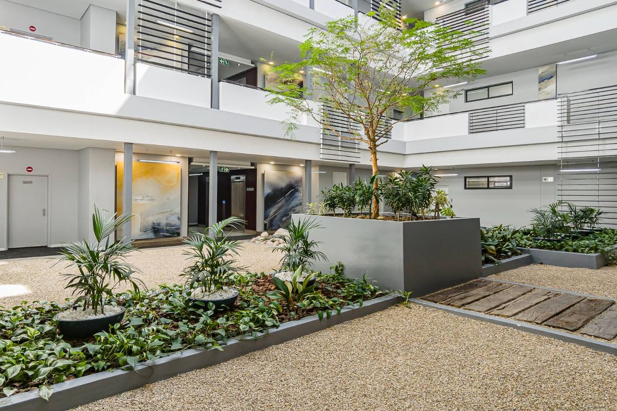 A well-maintained central atrium courtyard within an apartment complex, featuring landscaped garden beds, gravel pathways, and multi-level balcony access.