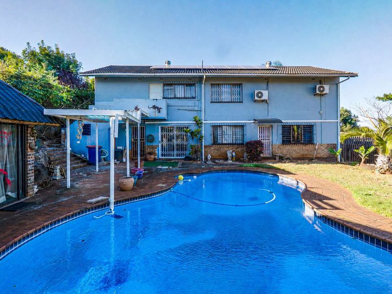 Rear exterior view of a two-story house featuring a swimming pool, paved patio area, and established garden space.