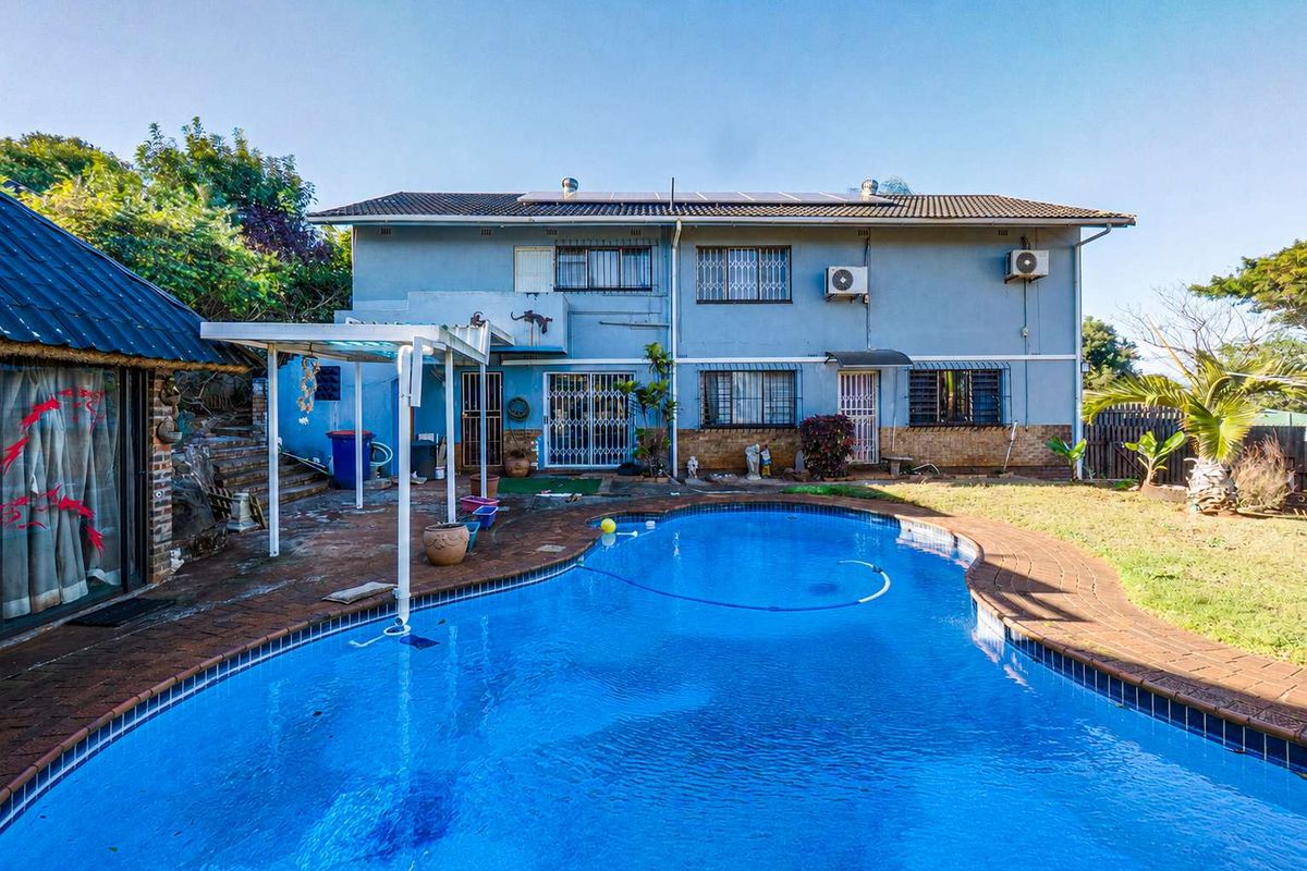 Rear exterior view of a two-story house featuring a swimming pool, paved patio area, and established garden space.