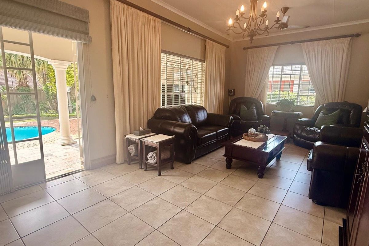 Spacious living room featuring large ceramic floor tiles, a classic chandelier, and sliding glass doors providing direct access to the patio and pool area.