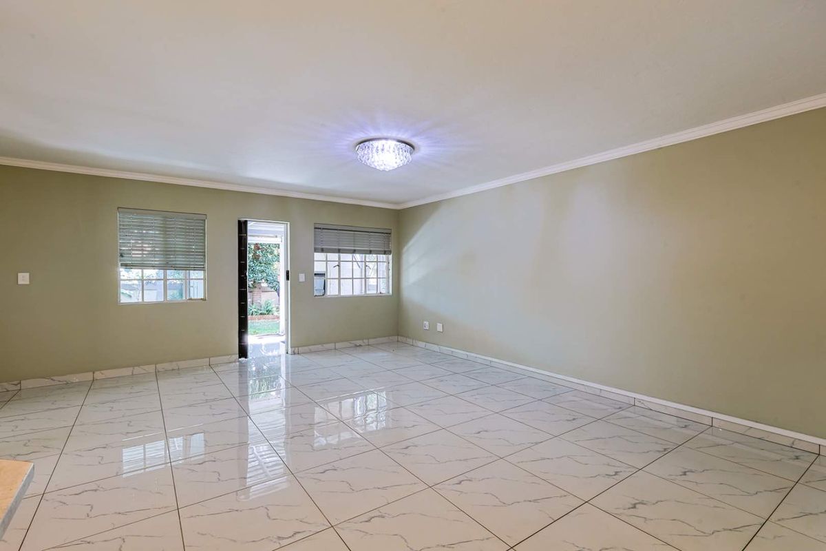 A spacious, empty living area featuring polished marble-look floor tiles, crown molding, and direct access to an outdoor space through a glass door.