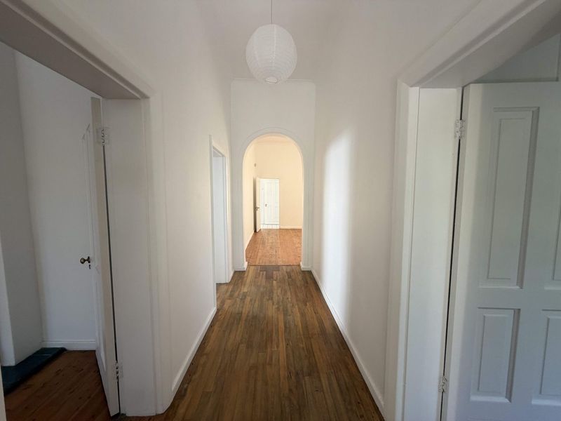 A bright, empty hallway featuring polished timber flooring and a classic architectural archway leading to adjacent rooms.