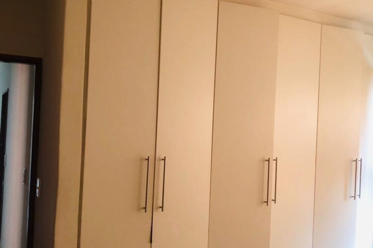 A bedroom featuring floor-to-ceiling built-in cupboards with modern handles, providing ample storage space.