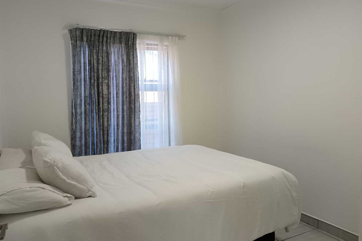 A simple bedroom featuring tiled flooring and a window with curtain tracks.