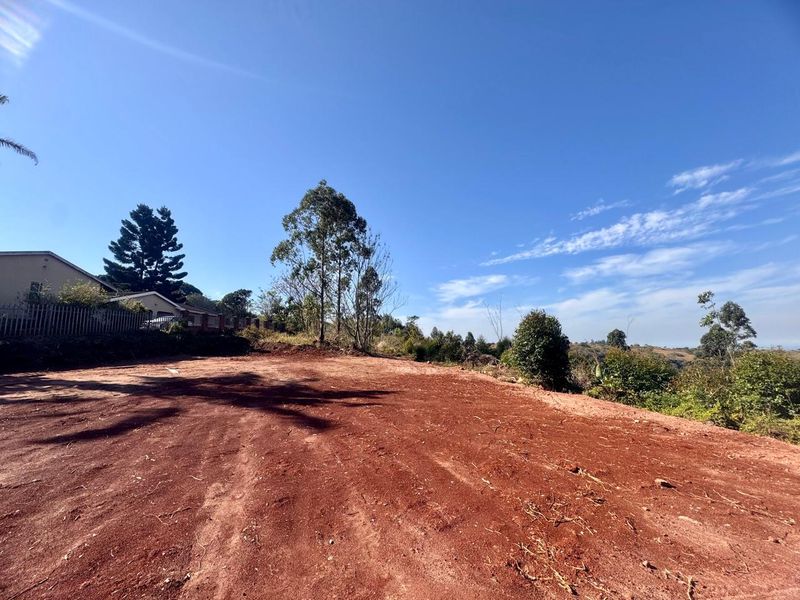 A vacant residential plot featuring cleared red earth, established trees, and perimeter fencing, offering a blank canvas for future development.