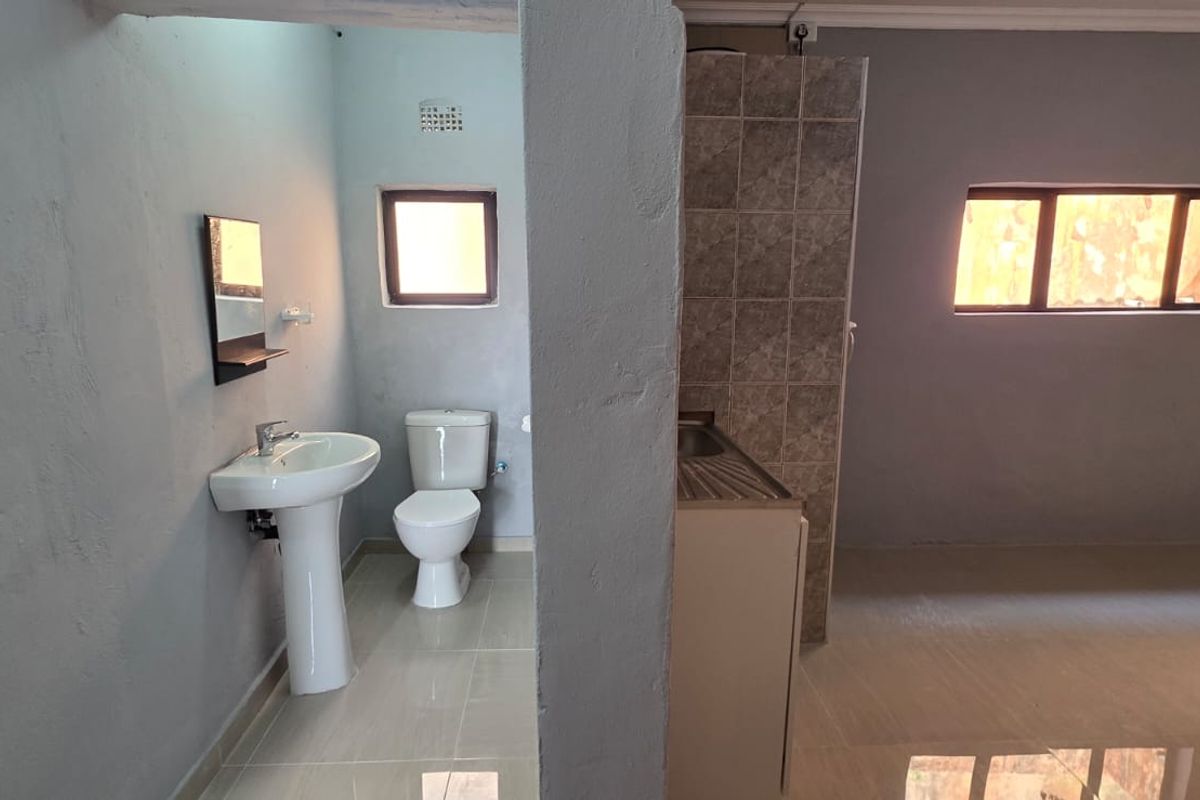 An open-plan studio apartment featuring a compact kitchenette area and a separate bathroom section with a pedestal basin and toilet.
